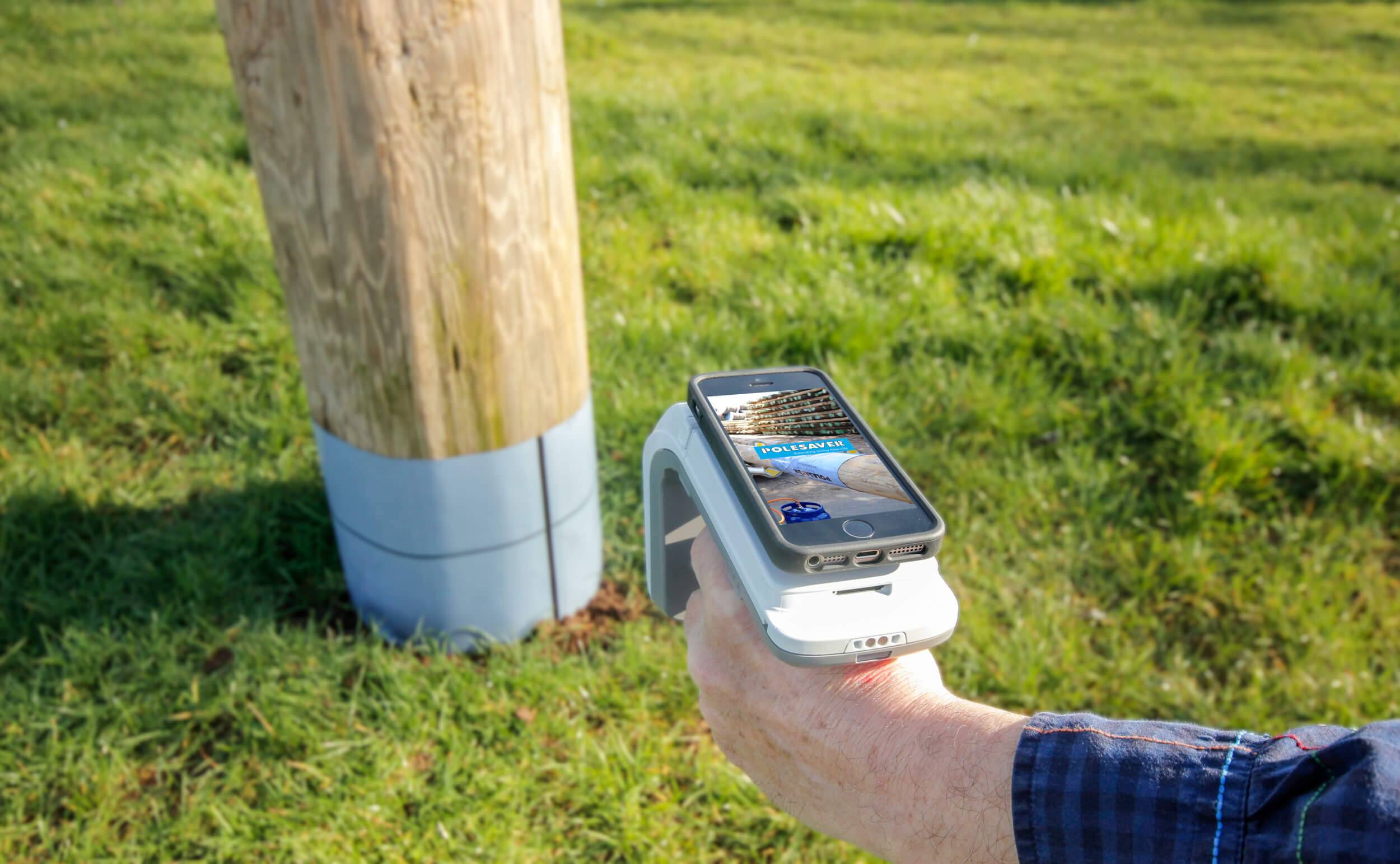 Polesaver RFID Asset Tracking Image Showing Smartphone attached to RFID reader pointed at a wooden utility pole with a polesaver sleeeve on Polesaver RFID Asset Tracking Image Showing Smartphone attached to RFID reader pointed at a wooden utility pole with a polesaver sleeve on